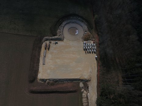 Ein Feld aus der Vogelperspektive. Das Feld ist teilweise umgegraben. Das Fundament für ein Windrad ist zu erkennen.