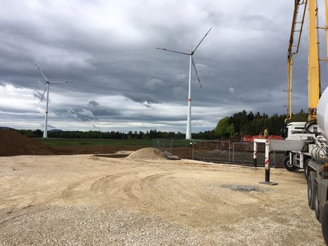 Baustelle mit zwei Windkraftanlagen im Hintergrund. Rechts ein Baufahrzeug.