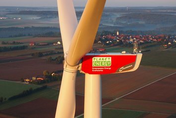 Luftaufnahme einer Windkraftanlage. Im Hintergrund bewirtschaftete Felder.