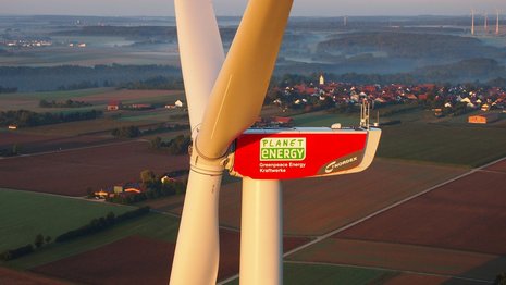 Luftaufnahme einer Windkraftanlage. Im Hintergrund bewirtschaftete Felder.