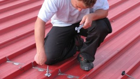 Arbeiter montiert Stockschrauben auf rotem Dach mit Schraubschlüssel