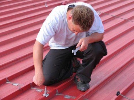Arbeiter montiert Stockschrauben auf rotem Dach mit Schraubschlüssel