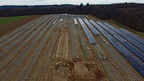 Braunes Feld mit Solaranlagen im Bau. Die Hälfte der Halterungen sind mit Solarpaneelen bestückt.