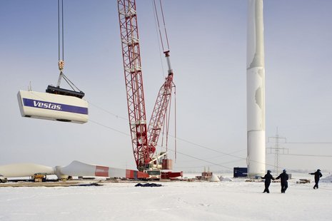 Der Rotor der Windkraftanlage wird von einem roten Kran angehoben. 3 Arbeiter halten den Rotor über 2 Seile stabil.