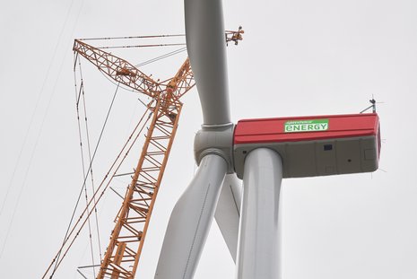 Windkraftanlage von unten angenommen. Daneben steht ein gelber Baukrahn.