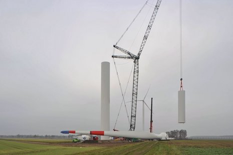 Ein Kran hebt einen Teil des Mastes der Windkraftanlage an, während ein Flügel im Vordergrund liegt.