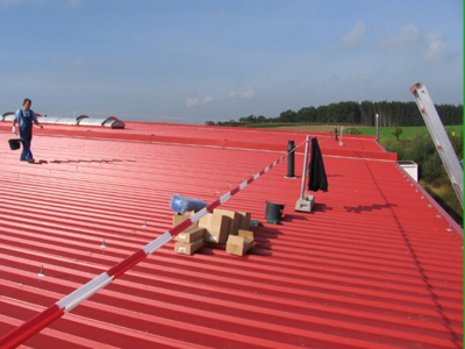 Rotes Dach, das teilweise abgesperrt wurde und auf dem ein Mann mit einem Eimer läuft