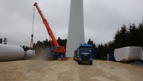 Baustelle zur Montage einer Windkraftanlage mit Kran und LKW im Vordergrund