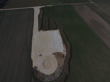 Ein Feld aus der Vogelperspektive. Das Feld ist teilweise umgegraben. Das Fundament für ein Windrad ist zu erkennen.