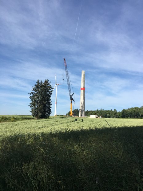 Bau einer Windkraftanlage auf einem Feld mit Kran und Windrad bei blauem Himmel.