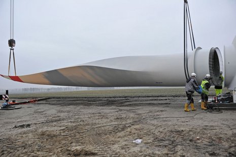 Drei Arbeiter montieren ein Windradflügel, der von zwei Seilen getragen wird.