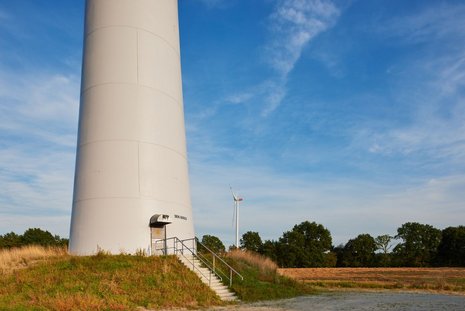 Windkraftanlage mit rotierenden Windrädern auf einem grünen Hügel.
