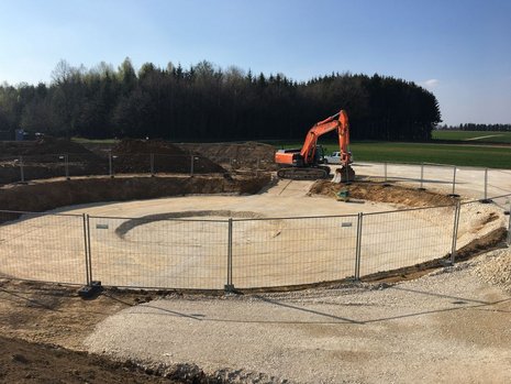 Rundes Erdloch mit Bagger bei der Arbeit im Hintergrund.