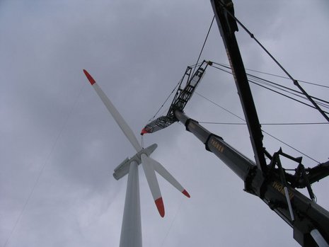 Bodenansicht der Montage von Windturbinenflügeln an einer Windturbine mit Hilfe eines schwarzen Krans.