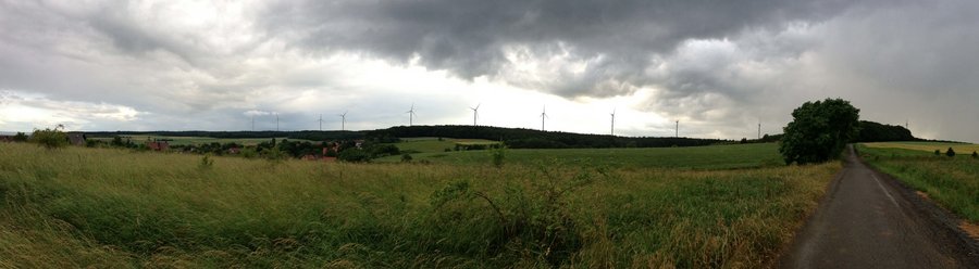 Panoramaaufnahme einer weitläufigen Landschaft mit mehreren Windkraftanlagen.