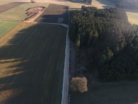 Felder aus der Vogelperspektive. In der Ferne ist eine Vertiefung im Boden. Die Erde wurde kreisförmig an den Rand geschoben. An diese grenzt ein umgegrabenes quadratisches Feld.