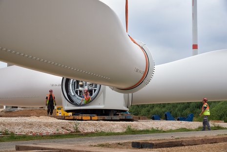 Montage des dritten Flügels an einer Windkraftanlage. Drei Arbeiter koordinieren den Vorgang.