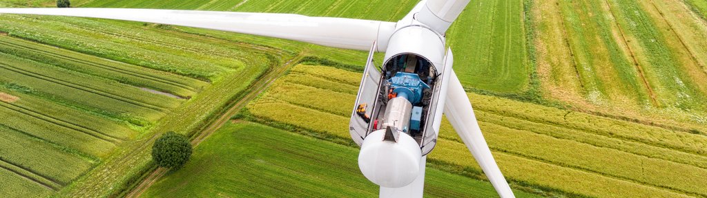 Geöffnete Gondel einer Windkraftanlage mit sichtbarer Technik, aufgenommen aus der Luft über grünen Feldern.