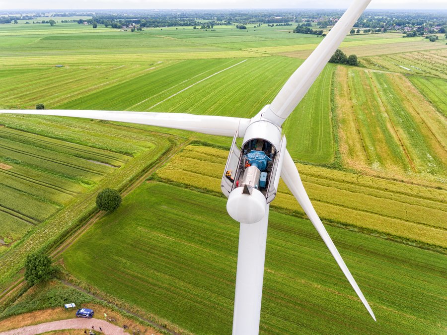 Geöffnete Gondel einer Windkraftanlage mit sichtbarer Technik, aufgenommen aus der Luft über grünen Feldern.