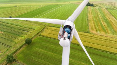 Geöffnete Gondel einer Windkraftanlage mit sichtbarer Technik, aufgenommen aus der Luft über grünen Feldern.