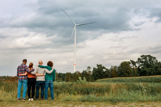 4 Personen beobachten in der Ferne eine Windkraftanlage, die sich inmitten eines Feldes erhebt.