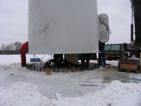 Windkraftanlage: Mast wird errichtet, Arbeiter montieren Teile.