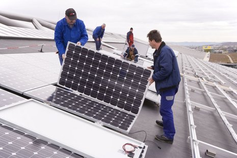 Zwei Arbeiter halten ein Photovoltaikmodul. Im Hintergrund haben Arbeiter gerade ein Modul in die Halterung gesetzt.