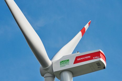 Nahaufnahme eines Windturms. Im Hintergrund ein klarer Himmel.