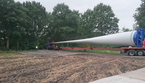 Ein Fahrzeug transportiert ein Windradblatt über ein Feld.