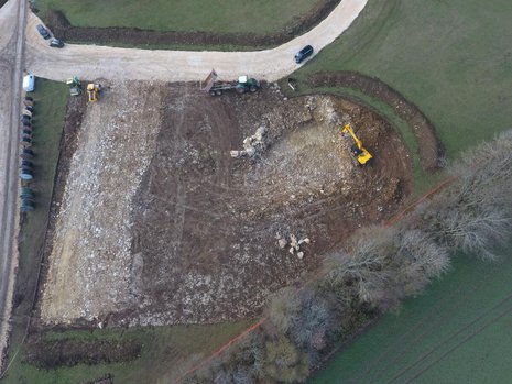 Ein Feld aus der Vogelperspektive. Ein Bagger gräbt den Boden auf.