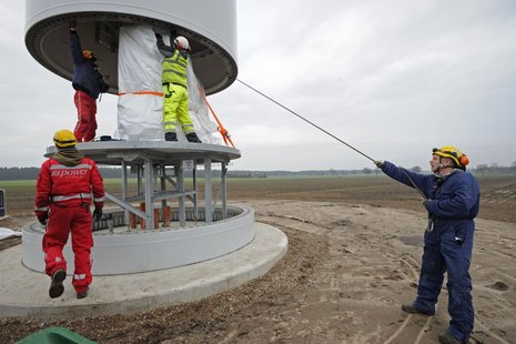 Montage des Windradmastes. 4 Arbeiter beaufsichtigen den Vorgang.