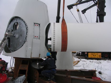 Montage eines Windradflügels. Ein Arbeiter überwacht die Installation.