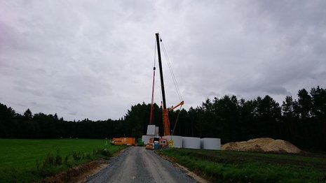 Ein roter Kran hebt einen Teil des Mastes der Windkraftanlage an. Im Hintergrund ein Wald