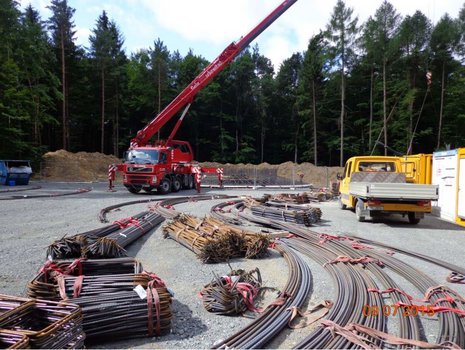 Ein Kran hebt Stahlstangen auf einer Baustelle.