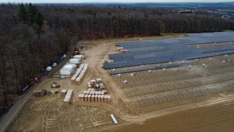 Braunes Feld wird mit Solaranlagen bebaut. Am Rand stehen Baumaterialien und Container.