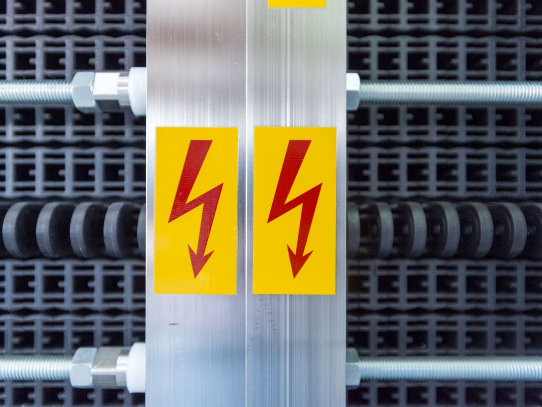 Elektrolyseur in der Nahansicht mit zwei Blitz-Symbolen als Zeichen für Hochspannung